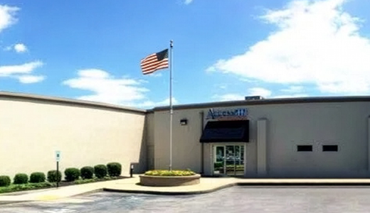 A commercial building with an American flag and well-maintained landscaping under a clear blue sky.