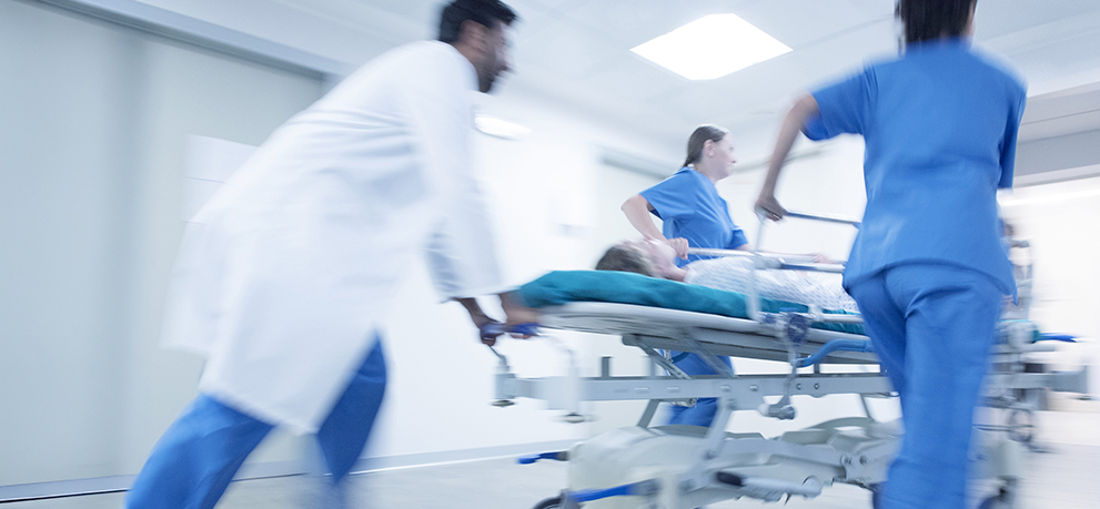 Medical staff rushing a patient on a stretcher in a hospital hallway.