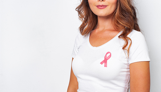 Woman in a white shirt wearing a pink breast cancer awareness ribbon on her chest.