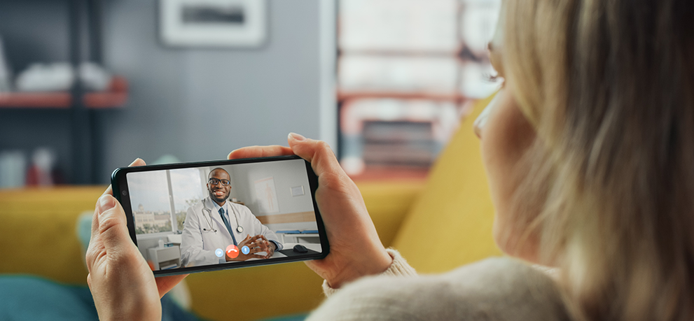 A person holds a smartphone showing a video call with a doctor in a white coat in a medical office.