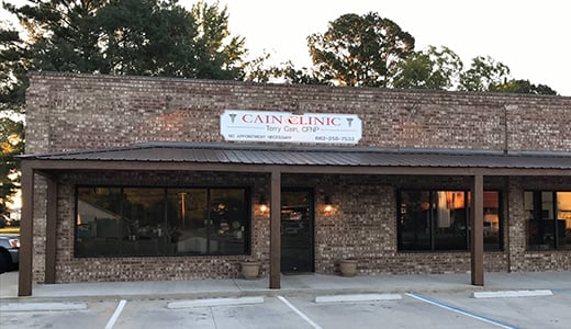 A brick building with a sign reading 'Cain Clinic' and an empty parking lot in the foreground.