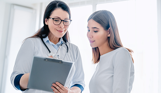 A healthcare professional discusses information with a person using a clipboard in a bright office setting.