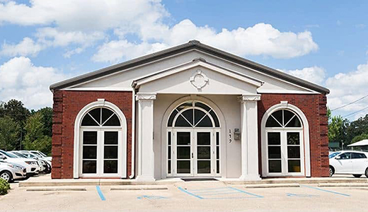 A brick and stone building with arched windows and a symmetrical facade under a blue sky.