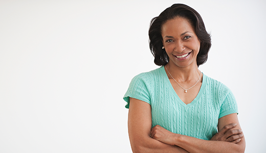A woman in a light green short-sleeve shirt smiles with arms crossed against a white background.