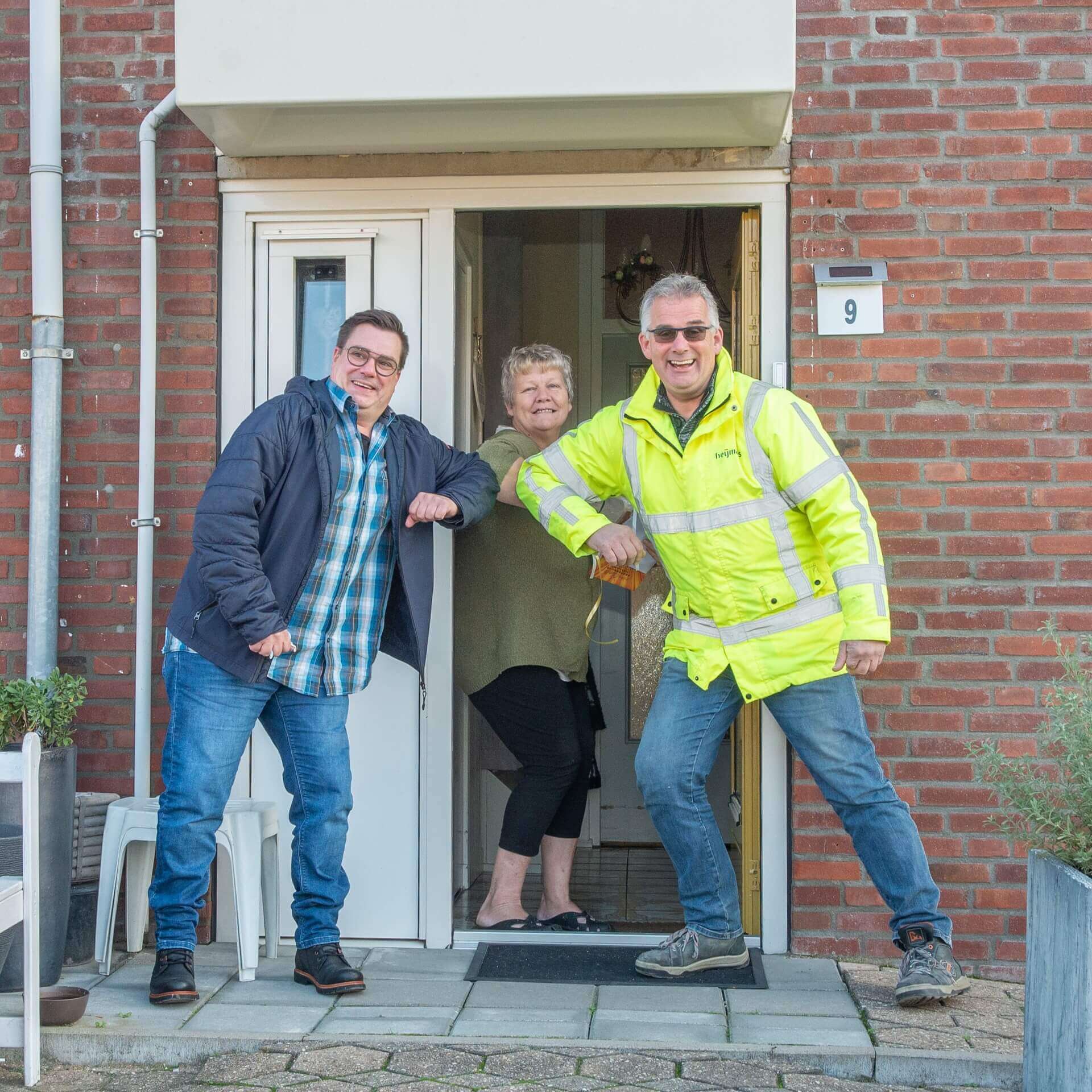 Three people engaging in a casual gesture near the entrance of a brick building.
